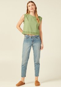 Top corto in cotone verde con bordo in pizzo, abbinato a jeans a vita alta blu chiaro e scarpe slip-on marroni. Design semplice, vestibilità casual.