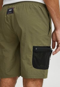 Grønne letvægtsshorts med elastisk talje, med en sort netlomme i siden og lynlås. Struktureret stof med glat overflade.