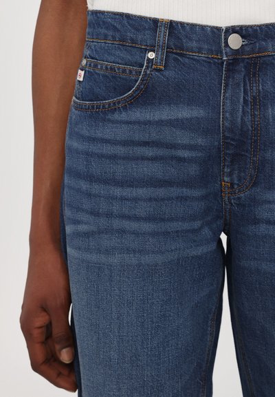 Jeans de mezclilla azul oscuro con una cintura alta, diseño de cinco bolsillos, costuras visibles y una pequeña etiqueta de la marca cerca del bolsillo delantero derecho.