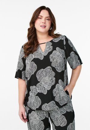 Haut noir avec motif floral blanc, manches courtes et décolleté en forme de clé. Tissu léger, avec une poche sur le côté.