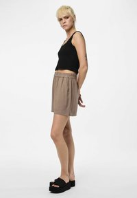 Débardeur noir côtelé et shorts beiges avec taille élastique. Modèle portant des sandales compensées noires, se tenant devant un fond blanc.