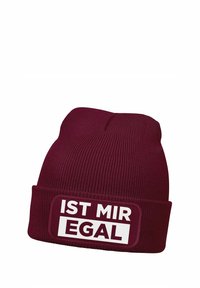 Maroon knit beanie with a cuff, featuring a white patch with the text “IST MIR EGAL.” The texture is ribbed, providing warmth and stretch.