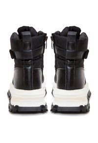 Bottes puffer noires avec une base en cuir lisse, un upper rembourré, une fermeture éclair et une semelle intermédiaire blanche épaisse avec une semelle extérieure noire texturée.