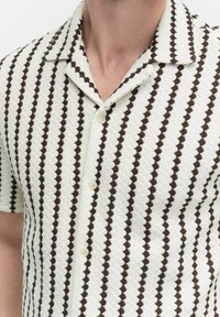 Korte mouw shirt in wit en bruin, met een gestructureerde stof met een ruitpatroon en een puntige kraag, vastgemaakt met lichte knopen.