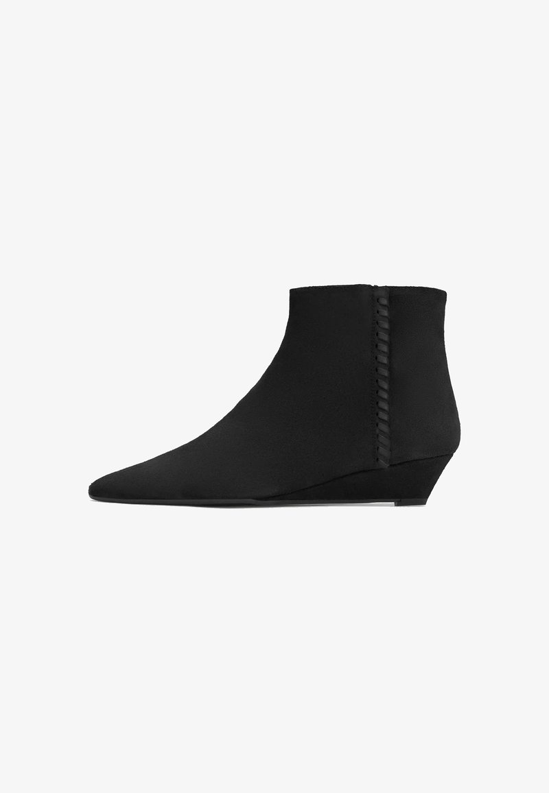 Bottine noire à cheville avec bout pointu, talon compensé bas et détail de bordure tressée le long de la couture latérale, vue de profil sur fond blanc.