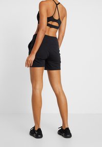 Mustat urheilushortsit, joissa on joustava vyötärö ja sivutaskut, yhdistettynä mustaan urheiluliiviin, jossa on leikkauksen muotoinen selkä.