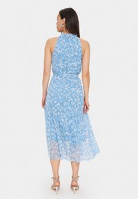 Rochie fără mâneci, de culoare albastru deschis, cu o siluetă fluidă. Se remarcă printr-o tivă în straturi și un model abstract subtil în nuanțe de albastru închis.