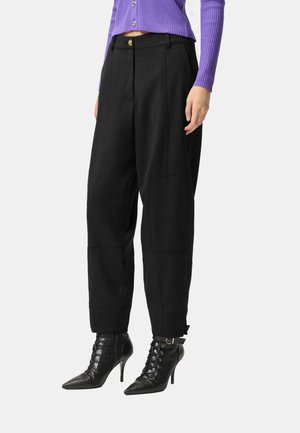 Pantaloni neri su misura a vita alta, con pieghe frontali e tasche laterali. Abbinati a stivaletti neri con lacci.