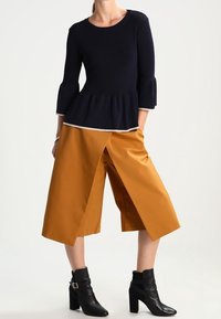 Granatowa bluzka peplum z dzwonowymi rękawami w połączeniu z musztardowymi culottes z rozcięciem z przodu, noszona z czarnymi botkami za kostkę z ozdobnymi klamrami.