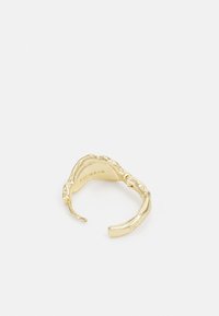 Bague en or avec un design texturé évoquant l'écorce, à extrémités ouvertes avec des bords lisses. À l'intérieur, le nom de la marque est gravé.