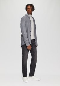 Grijze button-up overhemd over een witte coltrui, gecombineerd met donkere jeans en witte sneakers. Heeft lange mouwen en een comfortabele pasvorm.