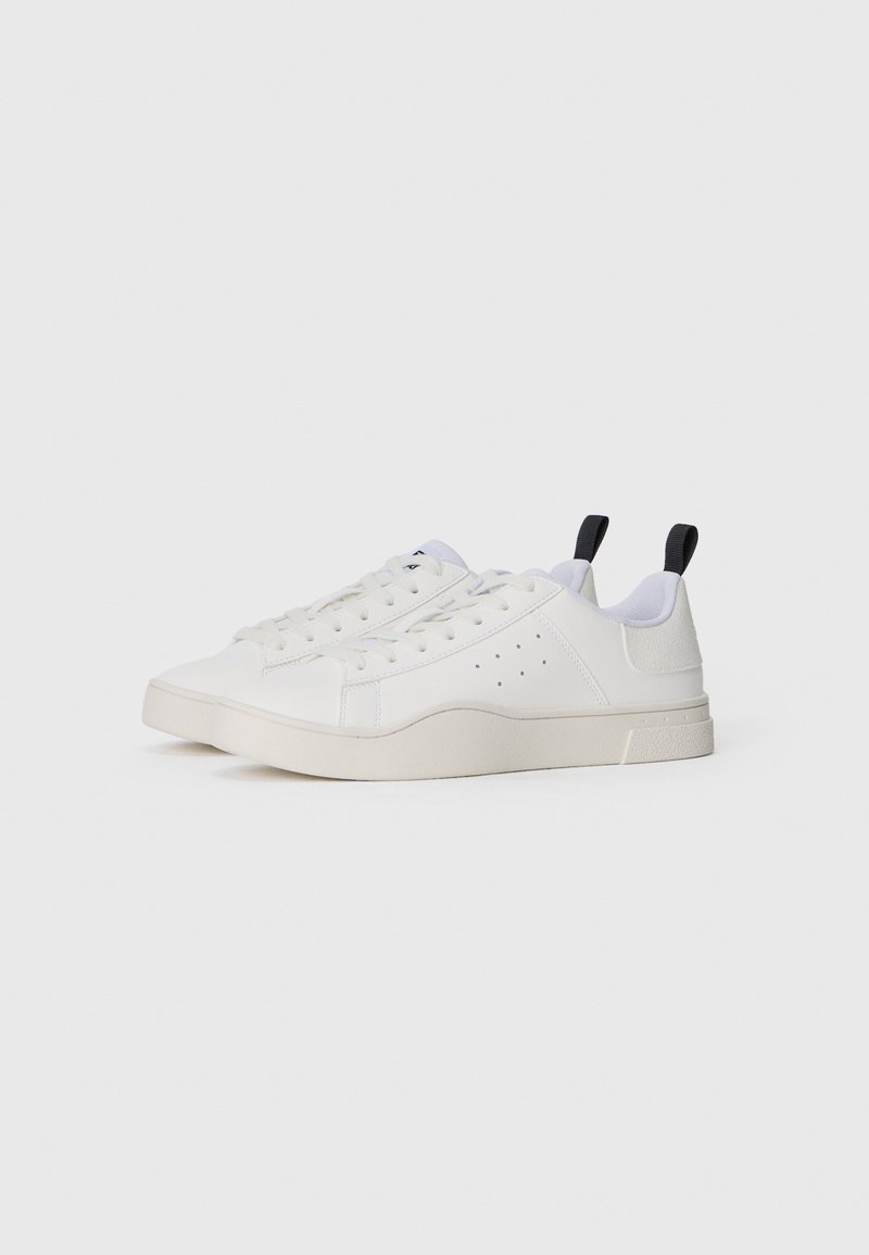 Zapatillas deportivas blancas con una textura suave, que cuentan con acentos perforados, suela plana y pestañas del talón en negro contrastante. Diseño clásico con cordones.