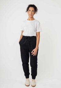 Weißes Baumwoll-T-Shirt kombiniert mit schwarzen Jogginghosen mit elastischem Bund und hellen Turnschuhen, mit einem lockeren Schnitt und seitlichen Taschen.