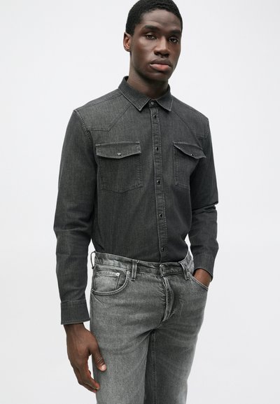 Camicia di denim grigio scuro con maniche lunghe, tasche sul petto e colletto, abbinata a jeans di denim grigio chiaro. Tessuto liscio.