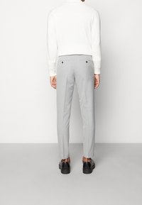 Jasnoszare dopasowane spodnie o gładkiej fakturze, z dwiema tylnymi kieszeniami z ciemnymi guzikami, w połączeniu z białą bluzką z długim rękawem.