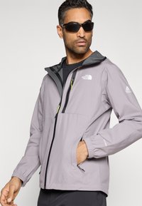 Ανοιχτό γκρι μπουφάν με φερμουάρ μπροστά, μαύρες λεπτομέρειες και ρυθμιζόμενη κουκούλα. Διαθέτει ελαστικά μανσέτα και δύο πλαϊνές τσέπες. Λογότυπο στο στήθος και στο μανίκι.