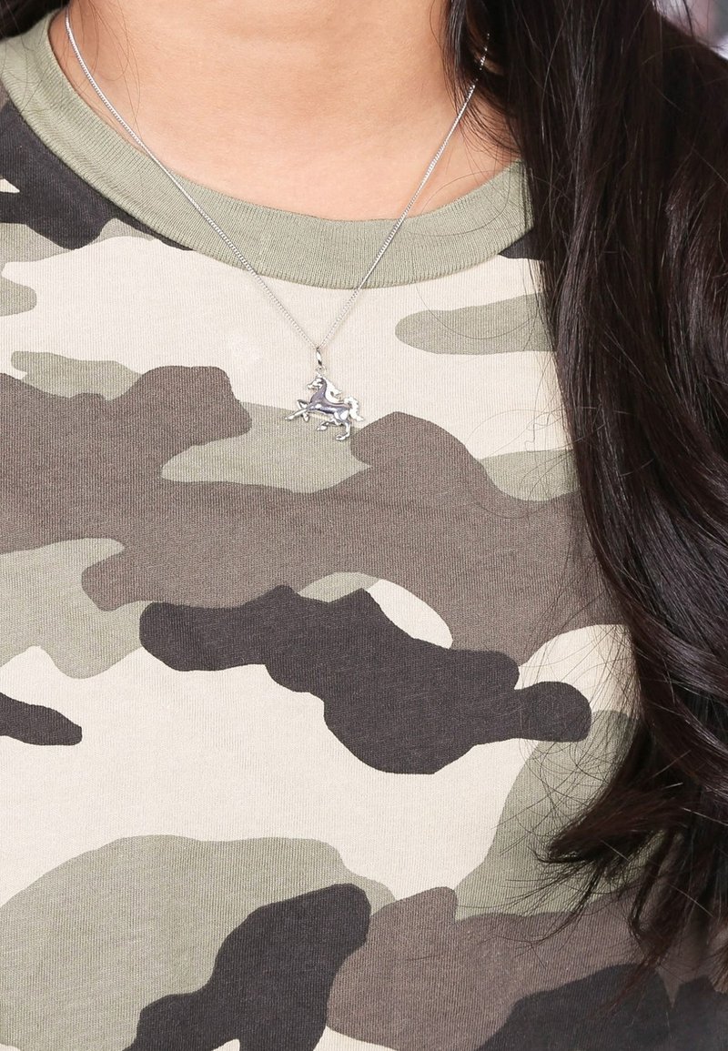 Silberne Halskette mit einem Anhänger in Form eines galoppierenden Pferdes, getragen über einem T-Shirt mit grünem und grauem Tarnmuster. Glatte Textilien mit taillierter Passform.