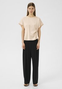 Haut en satin rose clair avec des manches courtes et larges, et un détail noué à l'avant, associé à un pantalon noir taille haute. Texture lisse, coupe décontractée.