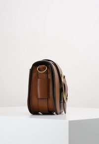 Brun läderväska med texturerad yta, rektangulär form och detaljer i guld. Har en sidstropp och en kontrasterande kant.