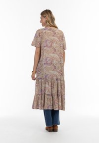 Brun kjole med paisley-mønster, korte ærmer og tiered ruffle kant. Båret med blå jeans og brune sko, set fra ryggen.