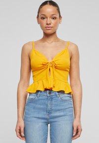 Žlutý pruhovaný crop top s tenkými ramínky, mělčí výstřih a zavazovací detail vpředu, s peplum lemem. Nosit s světle modrými džíny.