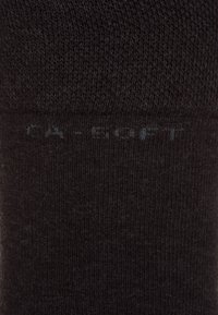 Schwarze Baumwollsocke mit ribbeliger Textur und glatter Oberfläche. Verfügt über ein dezentes "SOFT"-Label in Hellgrau nahe dem Bund.