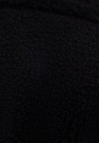 Czarna tkanina polarowa o miękkiej, teksturowanej powierzchni. Materiał wydaje się gruby i puszysty, o jednolitym kolorze, bez wzorów czy akcentów.