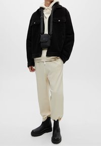 Giacca in velluto a coste nera sopra una felpa crema, abbinata a pantaloni felpati crema e stivali neri alla caviglia. Piccola borsa a tracolla nera con una cinghia.