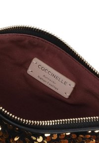 Sacchetto a forma circolare in paillettes dorate, zip nera, rivestimento bordeaux, con un'etichetta all'interno che segna "Coccinelle Autentico Cuoio Italiano."