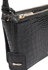 Zwarte lederen tas met krokodillenprint, voorzien van goudkleurige hardware, ritssluiting en een lange verstelbare schouderband. Compact rechthoekig design.