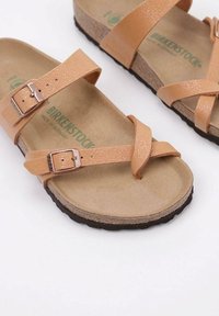 Birkenstock sandals with tan, textured synthetic straps, adjustable buckles, cork footbed, and black rubber outsole.