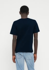 Μπλε ναυτικό βαμβακερό μπλουζάκι με κλασικό στρογγυλό λαιμό, κοντά μανίκια και άνετη εφαρμογή. Διαθέτει λείο ύφασμα και μινιμαλιστικό σχέδιο.