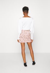 Parte superior blanca de manga larga con mangas abullonadas, combinada con una mini falda de estampado floral rosa y zapatillas negras. Diseño limpio y moderno.