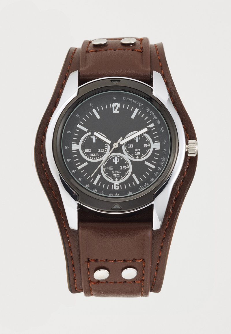 Montre analogique avec cadran noir, trois sous-cadrans, boîtier argenté et large bracelet en cuir marron avec surpiqûres orange et rivets métalliques.