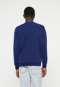 Sweatshirt bleu marine à manches longues, col ras du cou et poignets côtelés. Texture douce, design simple, apparaît décontracté et confortable.