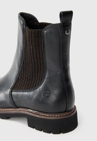 Bottine en cuir noir avec panneau latéral élastique, texture tissée marron, bout arrondi et semelle en caoutchouc texturé. Présente un logo près du talon.