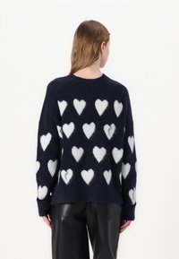 Maglione in lana blu navy con una consistenza morbida, decorato con motivi a cuore bianchi, colletto tondo e maniche lunghe.