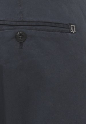 Tessuto blu scuro con bottone cucito e tasca orizzontale con cerniera dotata di piccolo tirante a forma di lettera "D" metallica.