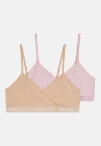 To bralette i beige og lys rosa, laget av myk stoff, med tynne stropper og et trykt "Converse"-logo på båndet.