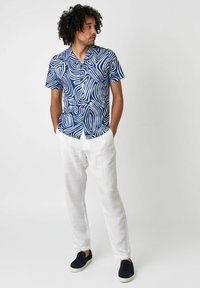 Kurzärmliges navy Hemd mit weißem abstrakten Muster, kombiniert mit hellen Leinenhosen und schwarzen Slippern. Lässige Passform und leichter Stoff.