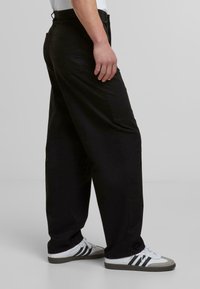Svarte chinos med en avslappet passform, synlige sømmer, side lommer og en glatt tekstur, kombinert med hvite joggesko med svarte striper.