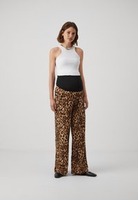 Bijeli top na haltericu s rebrastom teksturom, uparen s labavim hlačama s leopard uzorkom koje imaju crni pojas. Crne ravne cipele upotpunjuju izgled.