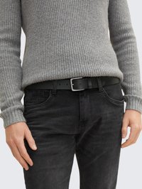 Maglione grigio a coste abbinato a jeans in denim nero, con cintura nera e fibbia argentata. L'outfit presenta uno stile testurizzato e casual.
