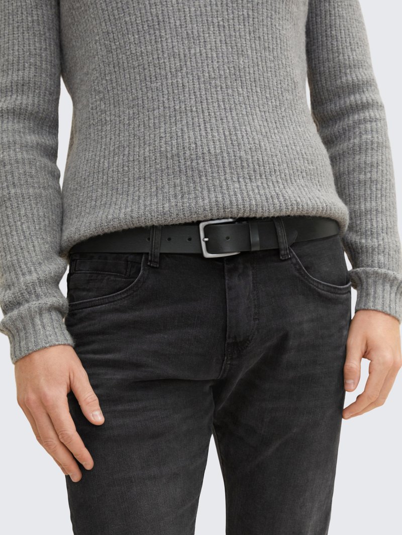 Maglione grigio a coste abbinato a jeans in denim nero, con cintura nera e fibbia argentata. L'outfit presenta uno stile testurizzato e casual.