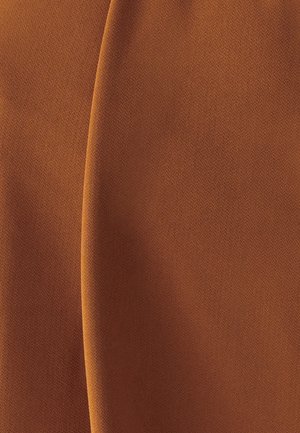 Smeđa teksturirana tkanina s vidljivom okomitom nabora koja stvara suptilne sjene i varijacije svjetla na površini tkanine.