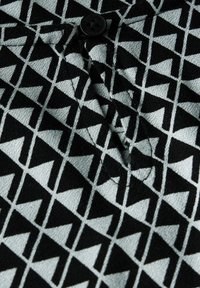 Tessuto nero e grigio con un motivo geometrico triangolare; presenta una chiusura con bottone; superficie testurizzata con dettagli di cucitura evidenti.