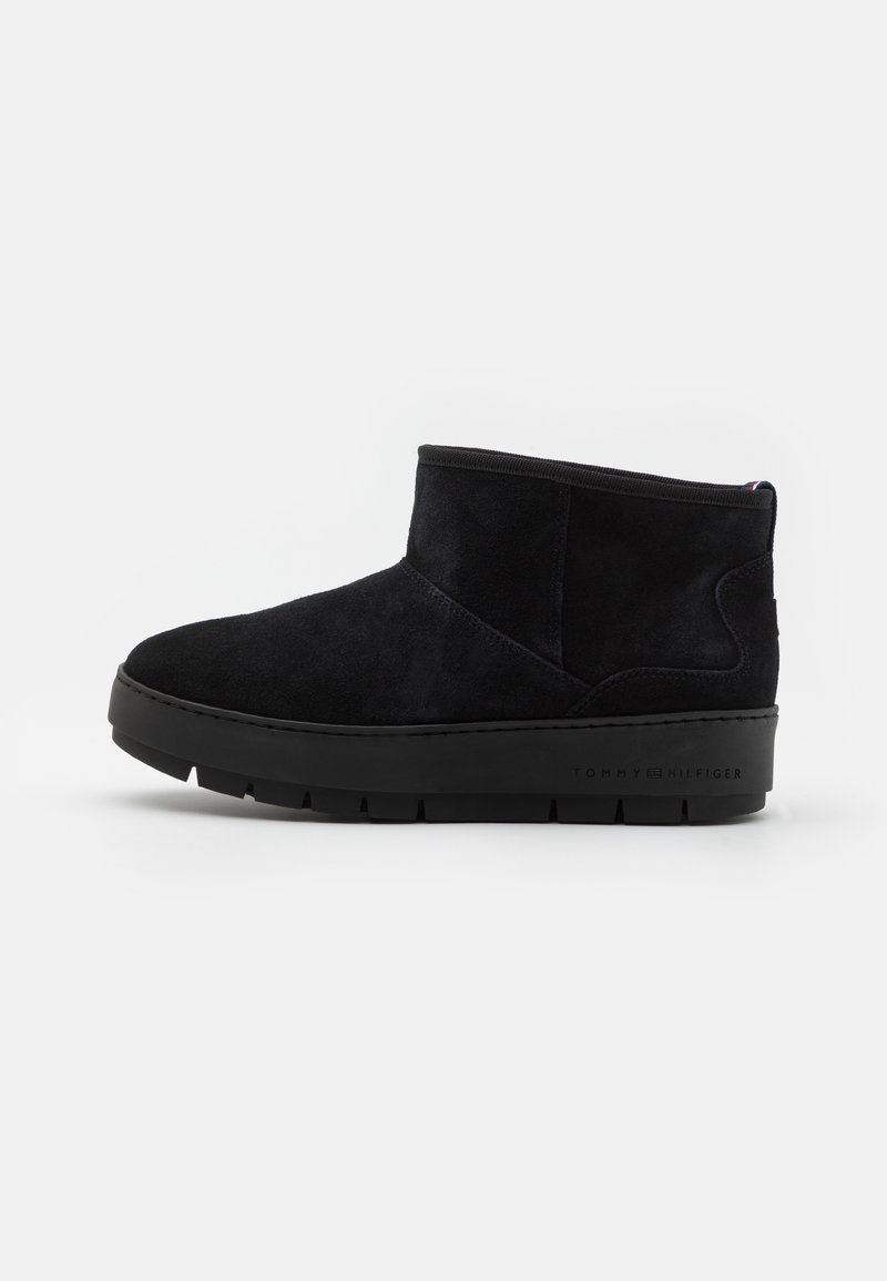 Bottes basses en daim noir avec bout rond, col élastique et semelle épaisse en caoutchouc noir avec le logo sur le côté.