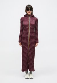 Langer, kastanienbrauner Steppmantel mit strukturiertem, gestepptem Design, durchgehendem Reißverschluss und Kapuze, mit einem kontrastierenden gelben Reißverschluss.