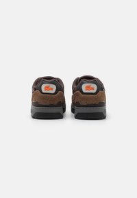 Braune Wildleder- und schwarze Mesh-Sneaker mit grauen Fersenakzenten und einem orangefarbenen Logo. Flache Gummisohlen mit strukturierten Mustern.