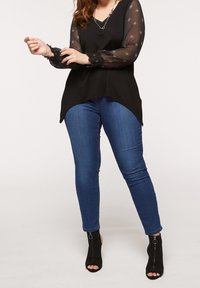 Black top with sheer, patterned long sleeves and a V-neckline. Paired with blue skinny jeans and black peep-toe ankle boots.